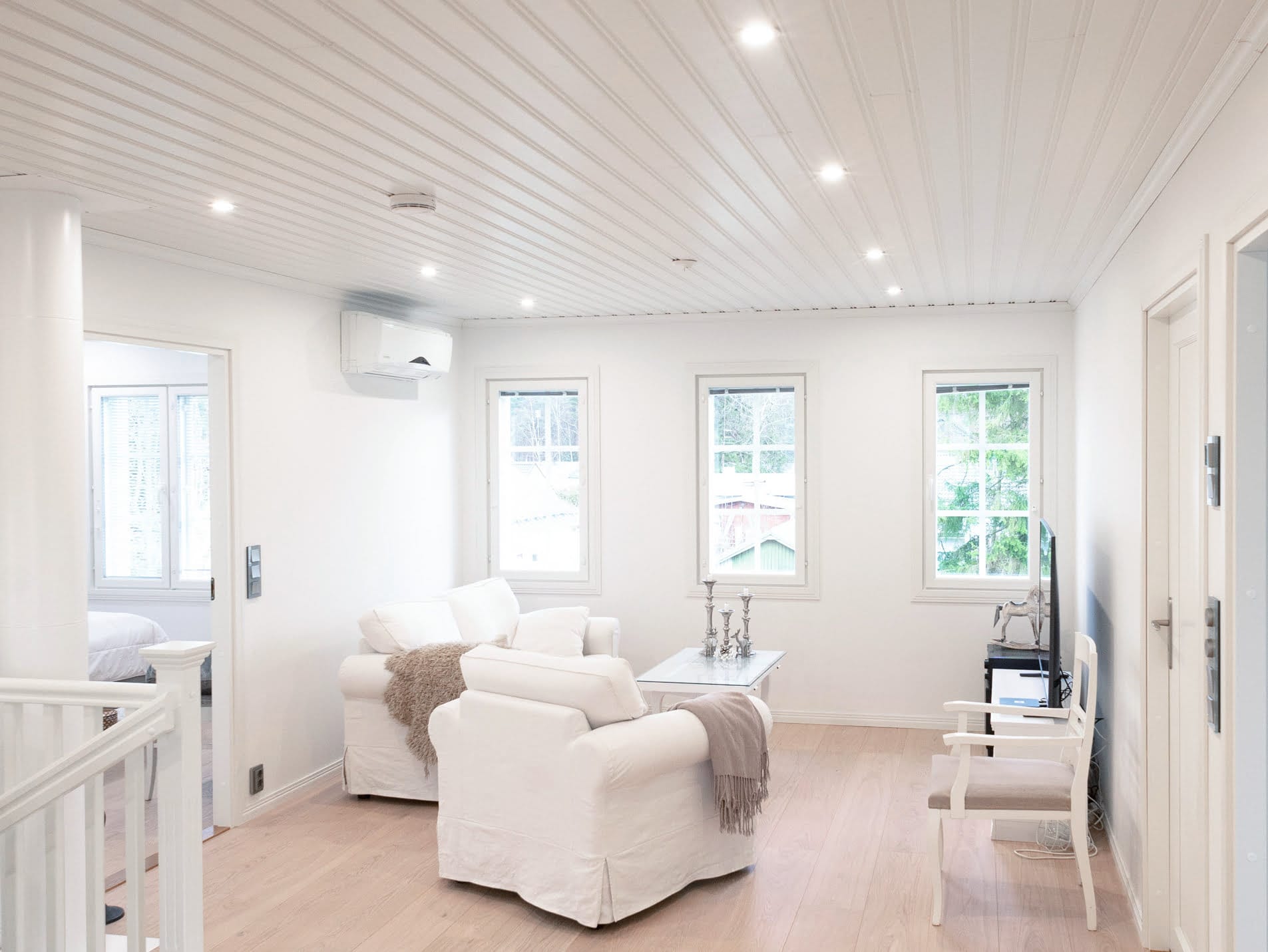 Blogin kansi 20.8.2021 - LedStore Moderni olohuone, jossa on LED-valaistus, valkoiset nojatuolit, sohvapöytä ja TV; lisää luonnonvaloa suurista ikkunoista ja korostaa puulattiaa.