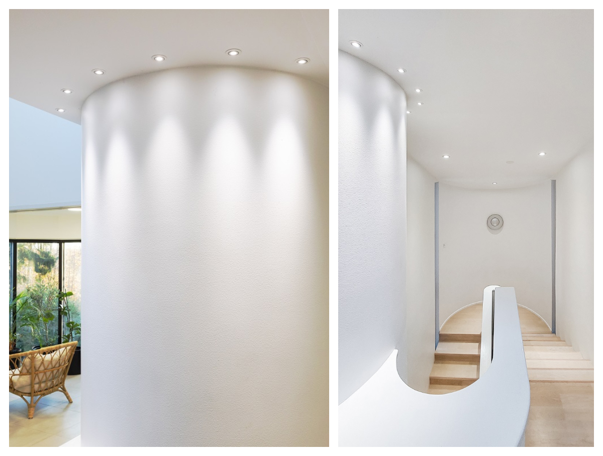 Moderni sisustus, jossa kaareva valkoinen seinä, jonka upotetut LedStore.fi:n led-alasvalot katossa sekä portaikko, jota korostavat luonnonvalo ja laadukkaat led-valaisimet – kokonaisuus luo harmonisen ja viihtyisän sisustusvalaistuksen. - LedStore Sisustuksellinen led-valaistus pienillä korostusspoteilla