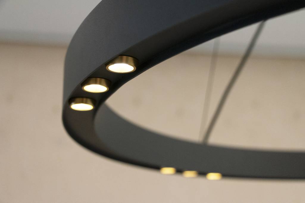 Lähikuva modernista mattamustasta pyöreästä kattokruunusta, jossa on upotetut LED-valot, jotka luovat pehmeää hehkua epäselvää taustaa vasten elegantin tunnelman luomiseksi.