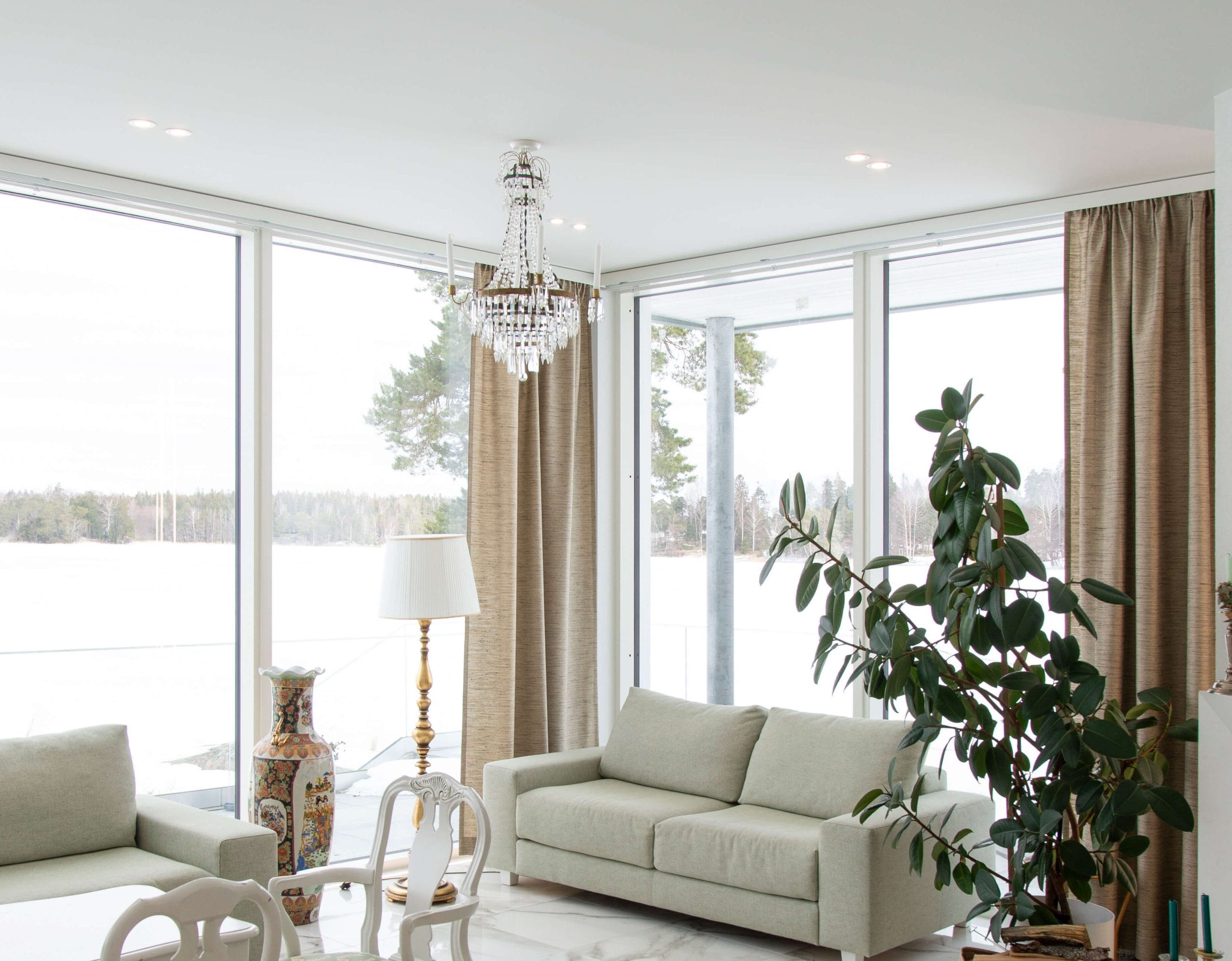 kansikuva OH - LedStore Valoisassa olohuoneessa, jossa on suuret ikkunat lumiseen maisemaan, on valkoinen sohva, suuri viherkasvi ja tyylikäs kattokruunu, jonka LED-valaisimet tuovat esiin sen kauneuden. Beiget verhot täydentävät koristeellista maljakkoa ja lattiavalaisinta, kun taas ruokapöytä valkoisine tuoleineen pilkahtelee taustalla. Tutustu LedStore.fi:n laajaan LED-valaisinvalikoimaan ja luo kotiisi yhtä upea valaistusratkaisu!